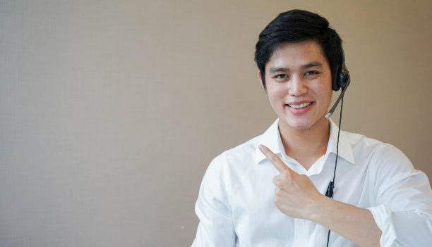 近距离年轻的呼叫中心员工微笑着戴耳机和手指向孤立在办公室空白背景客户关心和电话营销的工作概念图片下载