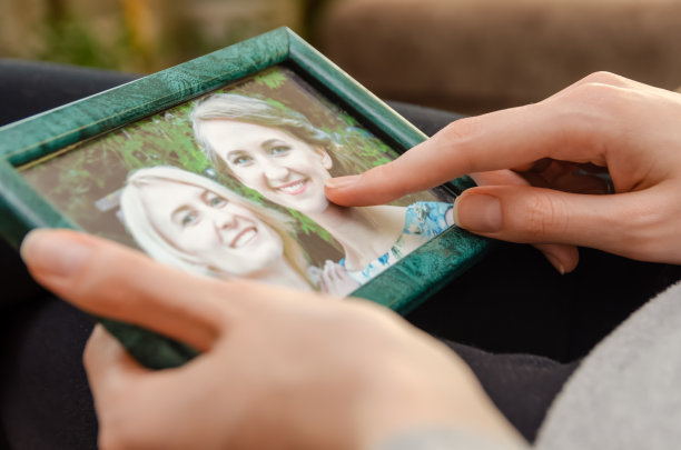 女孩手拿相框，框内是两个金发和棕发女孩的特写照片图片下载