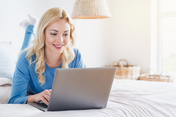 微笑的女人躺在床上，用她的笔记本电脑。在隔离禁闭中在家工作图片下载