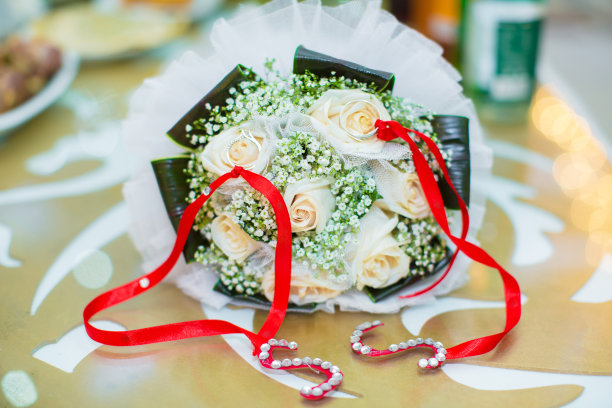 特写镜头。照片上没有人，只有金戒指和花。背景模糊。婚礼戒指戴在新娘的花束上，由粉色和白色的玫瑰组成。图片下载