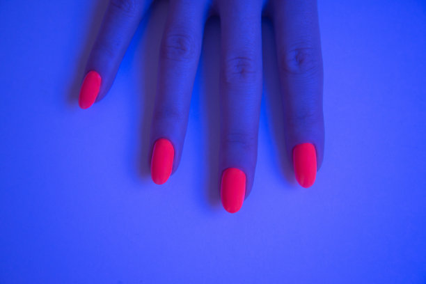 女人手与生动的橙色美甲在工作室霓虹蓝色的光。图片下载