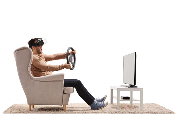 坐在扶手椅上的男人戴着虚拟现实耳机，在电视前握着方向盘图片下载