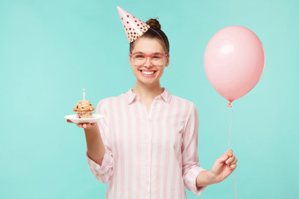 微笑的女孩手捧粉红色的气球和蛋糕庆祝生日，享受来自朋友们的惊喜，在薄荷蓝的背景下独处图片下载