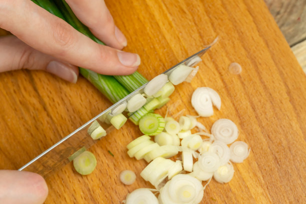 女人的手用刀在木板上切绿洋葱近看，看上面图片下载