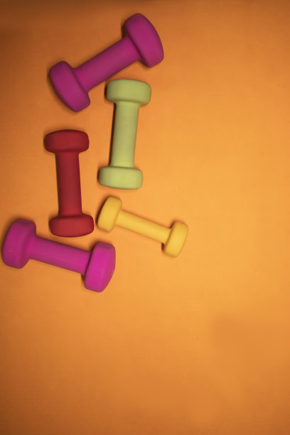 亮粉色，绿色，红色和黄色的小哑铃在橙色的背景上。体育的概念。图片下载