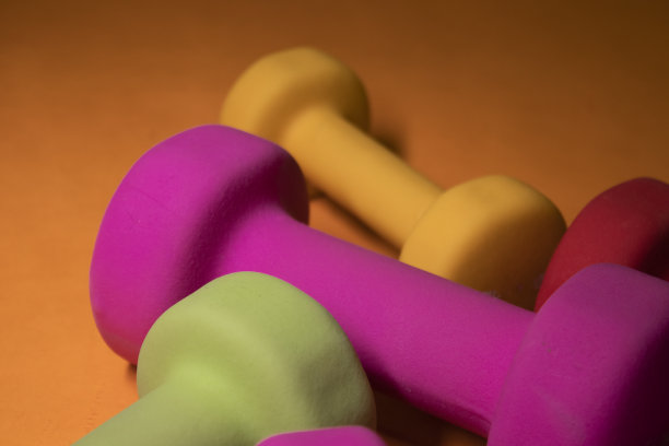 亮粉色，绿色，红色和黄色的小哑铃在橙色的背景上。体育的概念。图片下载