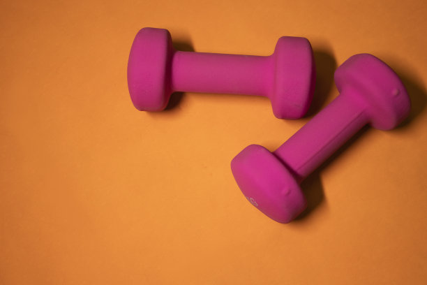 橙色背景上的亮粉色小哑铃。体育的概念。图片下载