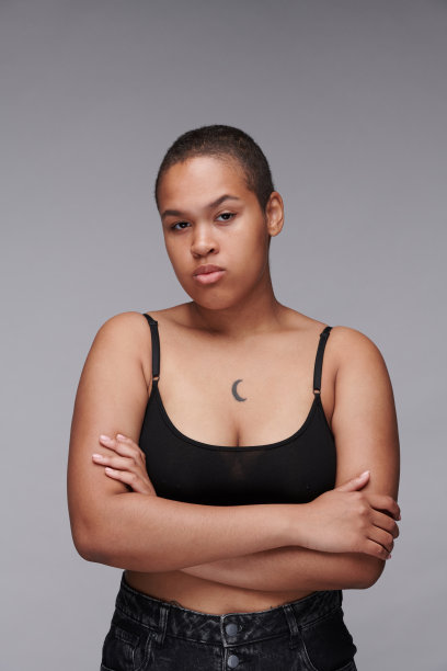 严肃的身体正面的黑人妇女的肖像与纹身站在交叉的胳膊对灰色的背景图片下载