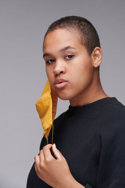 这是一幅短头发年轻黑人妇女的肖像，她的耳朵上挂着黄色的面具，背景是灰色的图片下载