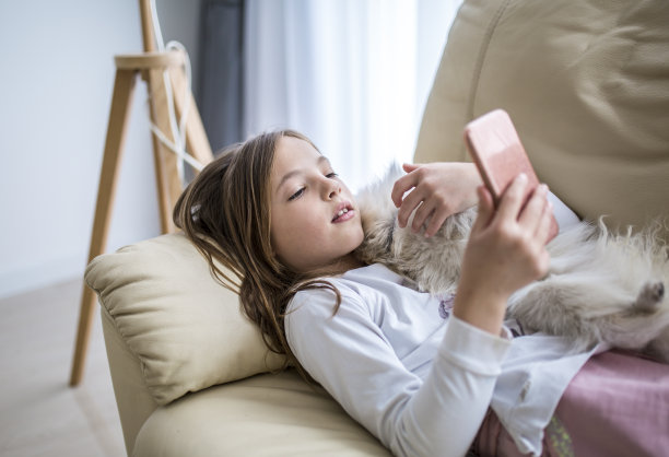 可爱的女孩躺在沙发上和她的狗，用手机在家库存照片图片下载