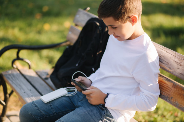 小男孩在智能手机上玩网络游戏，用充电宝充电。帅气的少年在一旁使用手机图片下载