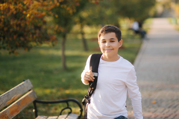 男学生早上去上学。快乐少年穿着白衬衫背着黑背包去学习图片下载