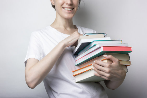 一个穿着白色t恤的女孩手里拿着很多书，背景是中性的。教育、培训手册图片下载
