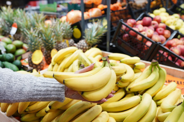女孩用手从商店的货架上拿香蕉。健康食品。购物的概念图片下载