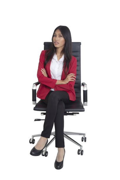穿着红色套装的女商人双臂交叉坐在黑色的扶手椅上。图片下载