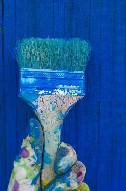 戴着手套的手拿着刷子，背景是蓝色的木头，有复印空间。自己动手DIY的概念。房子装修。图片下载