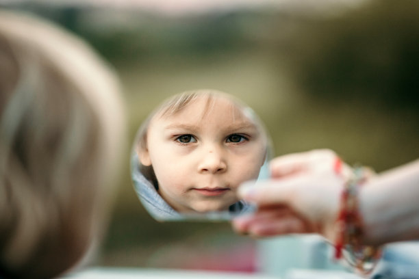 一个可爱的蹒跚学步的小男孩，看着镜子里的孩子图片下载