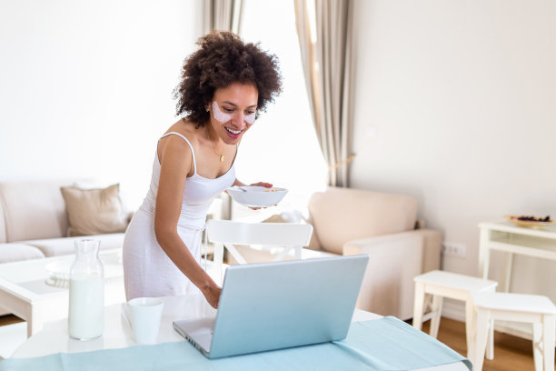 美丽的年轻女子喜欢吃玉米片作为早餐，同时在她的笔记本电脑上工作。图片下载