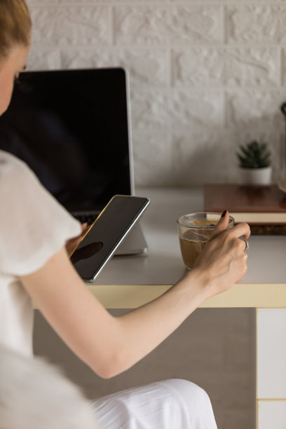 一个面面俱到的年轻女子在家工作，一边喝咖啡一边给朋友发短信图片下载