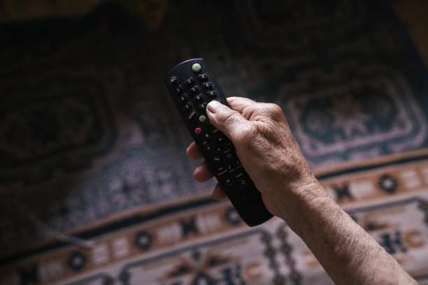 POV，一个妇女的手满皱纹使用遥控器的特写。祖母在换电视频道。新冠肺炎期间看电视的老年妇女。图片下载