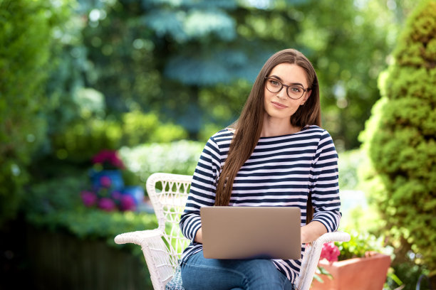 微笑的年轻女子使用笔记本电脑在家里的花园里图片下载