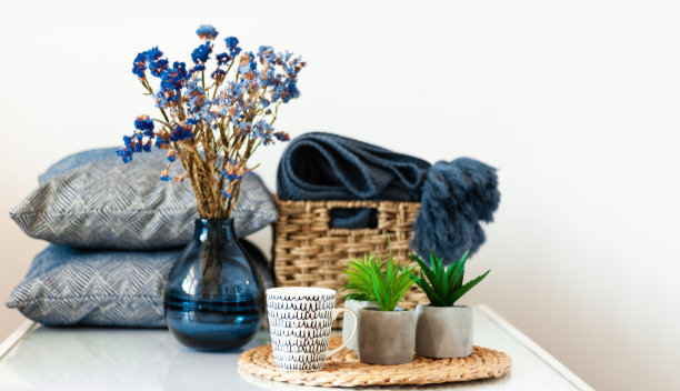 舒适的室内装饰:咖啡杯，枕头，格子，花瓶与花，植物在花盆上的柳条架上的白色架子在房间里。待在家里的隔离概念。图片下载