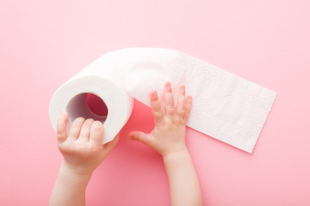小女孩双手捧着柔软的，白色的卫生纸卷在浅粉色的桌子背景上。柔和的颜色。卫生的概念。特写镜头。视角拍摄。自顶向下的观点。图片下载