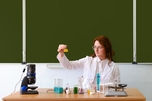 学校化学老师在课堂上公开上课，生活方式。一位女士在讲台上拿着一瓶化学溶液图片下载