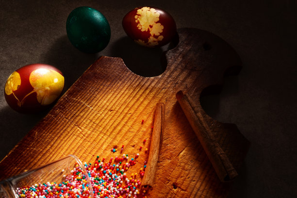用来装饰蛋糕的彩色糖果从旧厨房木板上的玻璃杯里溢出来，还有彩色鸡蛋和肉桂棒。有选择性的重点。复活节和家庭面包房假日概念照片。图片下载