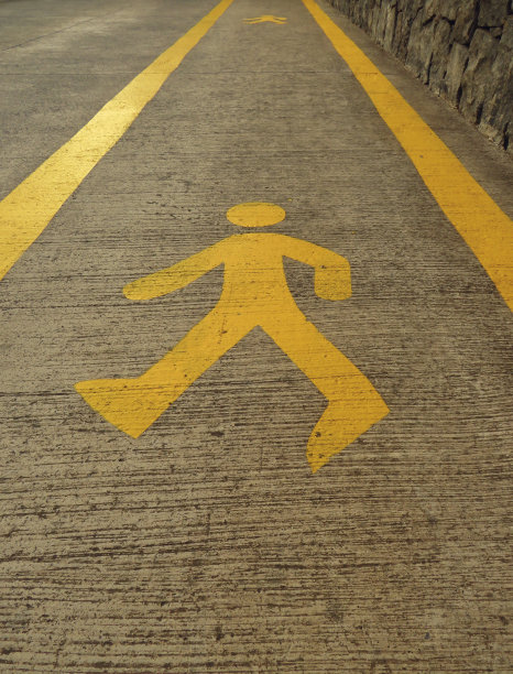 人行道上黄色行人标志的背景。近景的行人行走的数字画标志图标符号在黄色油漆黑色沥青人行道。图片下载