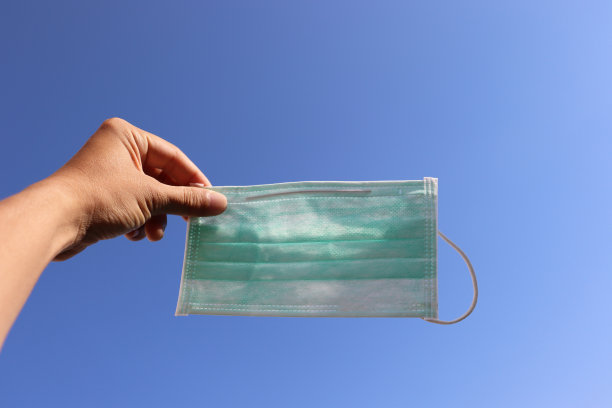 一只手拿着口罩带着蓝天。图片下载