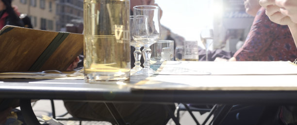 户外餐厅餐桌的透视视图。等待秩序的人们。他们会先看菜单和价目表，然后再点餐。桌上有散装的酒瓶和酒杯。在户外吃喝。图片下载