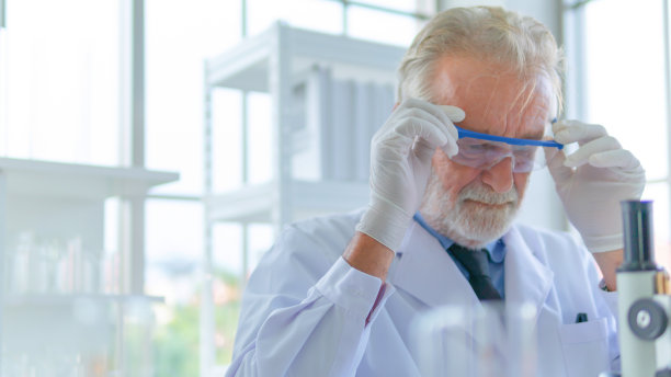 资深教授男研究员一心想着实验室测试科学。室内白色实验室，桌上有设备。图片下载