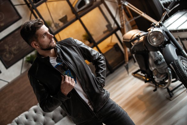 完美的男人。穿着皮夹克的年轻潮人站在房间里。图片下载