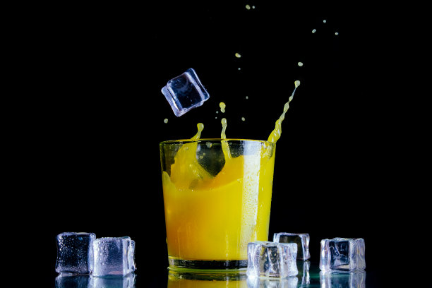 在一个透明的玻璃杯中洒上橙汁和冰块，背景是黑色的图片下载
