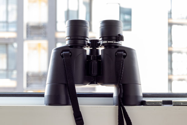 一种黑色的双筒望远镜，以模糊的窗户背景为背景，观察邻居、环境或自然。有选择性的重点。特写视图图片下载
