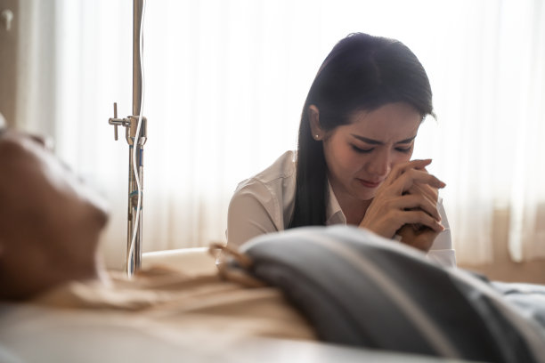 亚洲病人男子躺在病床上重病在恢复室的医院手术后，妻子坐在和照顾。女人压力大，担心丈夫的症状，牵着手低下头哭泣。图片下载