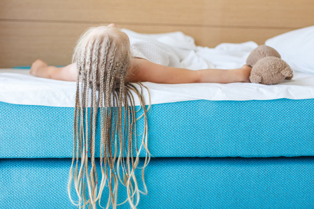 一个梳着金色长辫子的女孩躺在绿松石色的床上，盖着一条白色的毯子，双手放在床边，一只泰迪熊。回家,休息,早上在酒店图片下载