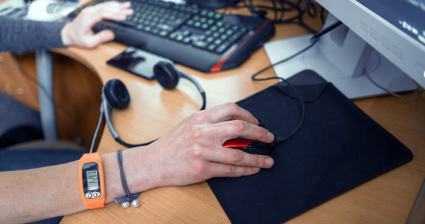 手握健身手环在电脑前工作的女孩。特写镜头。女孩的手在键盘和鼠标在桌子上。电脑工作概念图图片下载