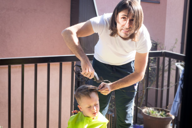 在隔离和自我隔离期间，爸爸在阳台上给小儿子理发。图片下载