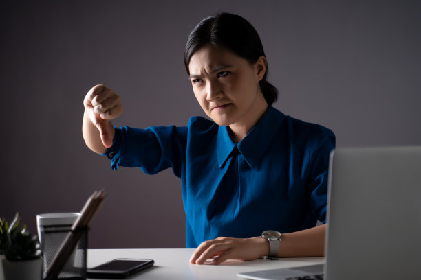 一名穿着蓝色衬衫的亚洲女性很生气，并在办公室用笔记本电脑工作。孤立的背景。图片下载
