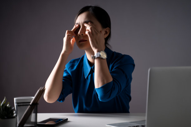 一名身穿蓝色衬衫的亚洲女子因在办公室使用笔记本电脑而眼疼。孤立在白色背景上。图片下载