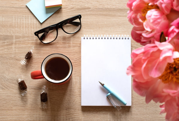 一张轻木桌子上的静物画。一个白色的记事本，一杯茶，鲜花。图片下载