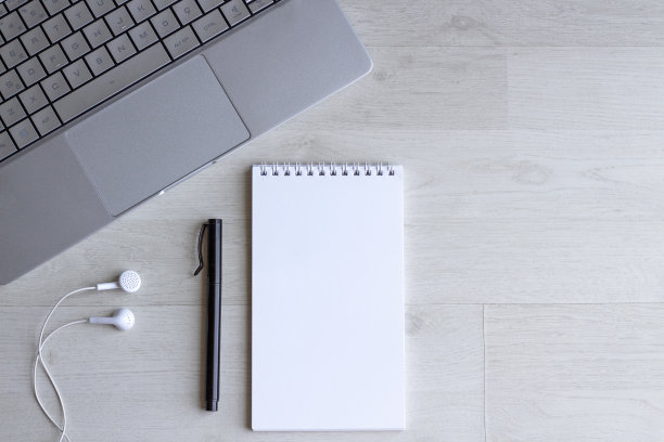 办公桌桌上有空白笔记本，钢笔，电脑键盘和耳机。图片下载