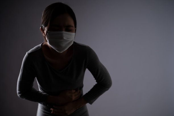 一名亚洲妇女戴着防护面罩，因胃痛而不适，双手按在孤立的腹部上。图片下载