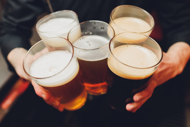 朋友们拿着啤酒杯围坐在咖啡馆酒吧的桌子旁欢呼。一群不同种族的人在酒吧里互相敬酒碰杯。图片下载