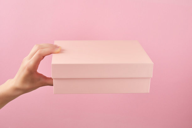 女人手握粉红色的盒子在粉红色的墙壁背景与复制空间。包裹递送的概念图片下载