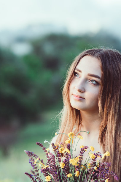 美丽的女孩与野花在草地上，年轻的女人长头发穿着衣服走在自然，夏天温柔的照片在村庄图片下载
