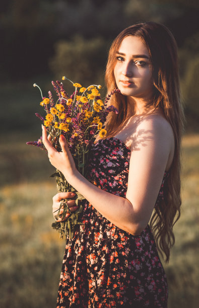 美丽的女孩与野花在草地上，年轻的女人长头发穿着衣服走在自然，夏天温柔的照片在村庄图片下载