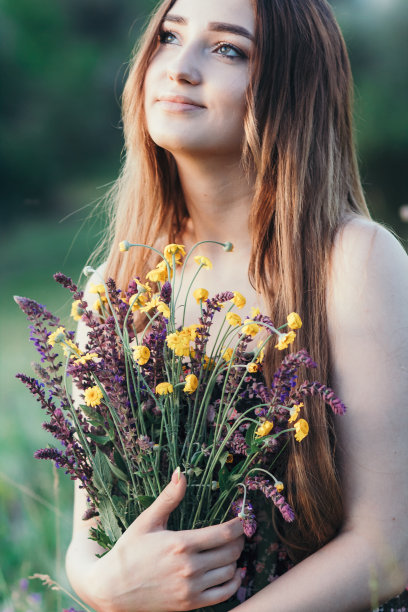美丽的女孩与野花在草地上，年轻的女人长头发穿着衣服走在自然，夏天温柔的照片在村庄图片下载